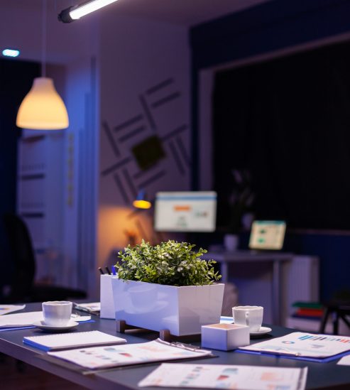 Modern empty business corporate office meeting room is ready for businesspeople late at night. In background on conference table standing company financial documents with economy graphs